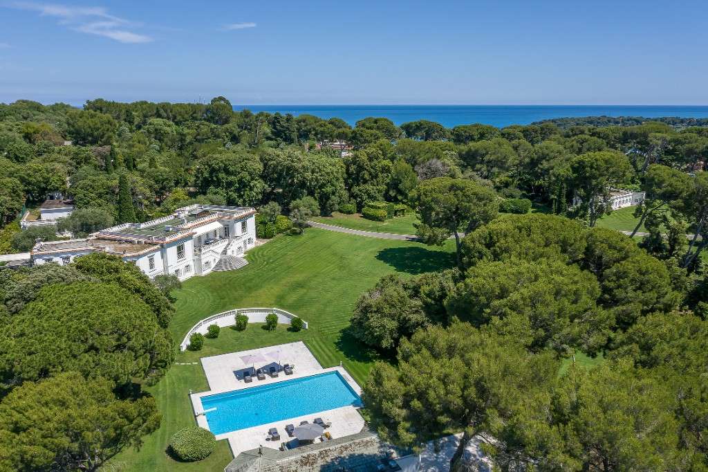 Vue aérienne de la villa, de ses pelouses et de la piscine parmi les pins parasols, avec la Méditerranée au loin